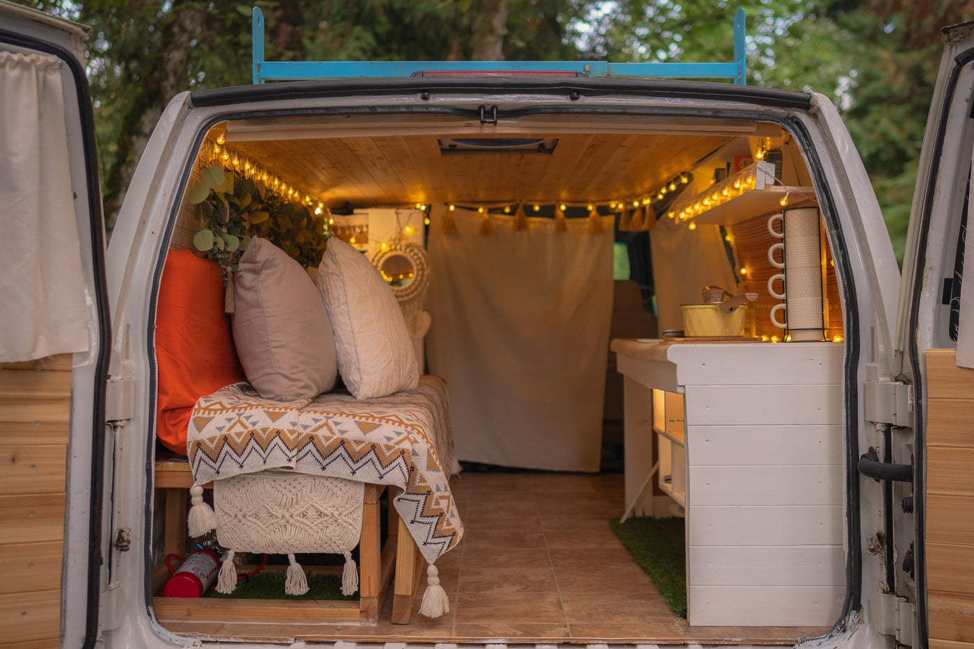 Cozy RV rental van conversion interior with a bench, kitchen, and warm string lights. Perfect for camper adventures. — photo 5