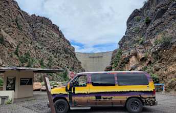  ideal for camping adventures. A small dog is nearby.|Explore stunning canyons with an RV rental! Colorful camper van parked before a massive concrete dam within steep — photo 4