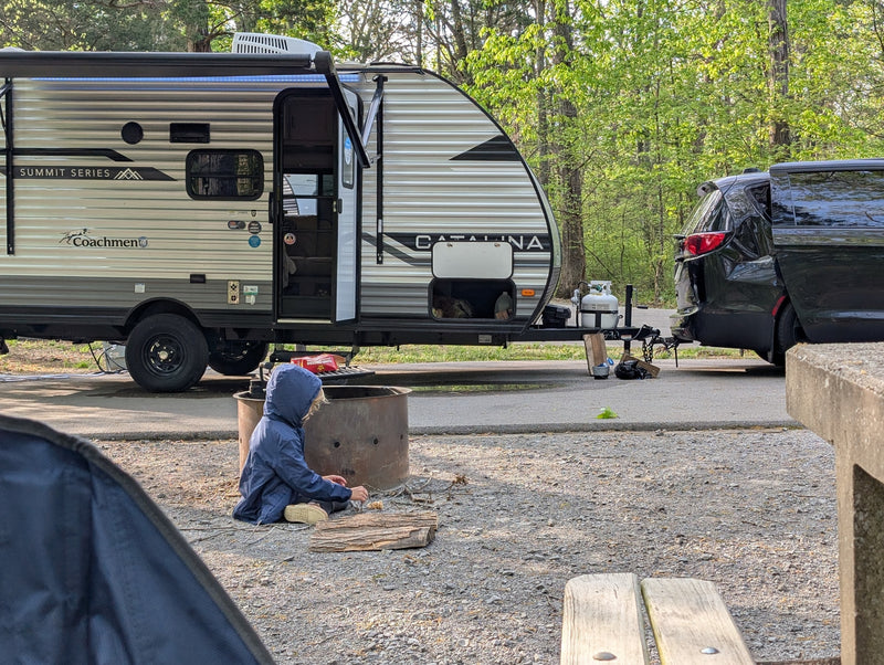 A child prepares kindling by a fire pit at a Coachmen Catalina travel trailer RV rental campsite. — photo 12