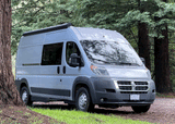 This grey Ram ProMaster rv rental camper van is perfectly parked in a towering redwood forest, ready for your outdoor adventure.