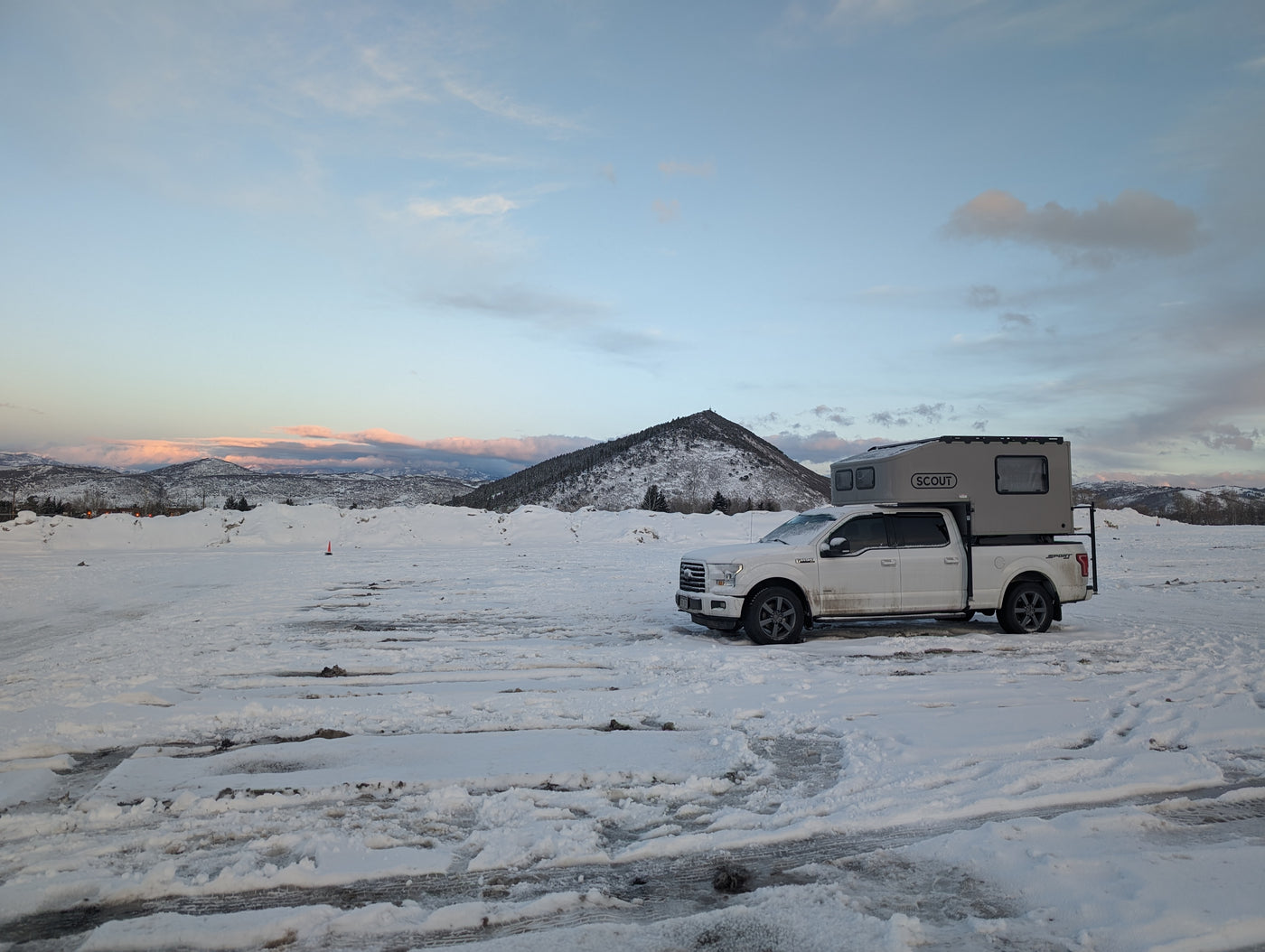 A white Ford pickup with a grey Scout truck camper is parked on a snowy plain with mountains in the background. Consider an RV rental for winter camping. — photo 20