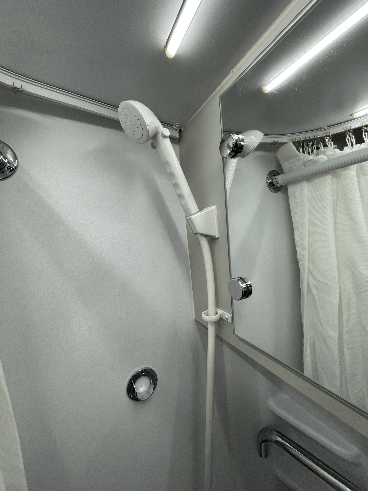 Compact shower in an RV rental, featuring a handheld showerhead, mirror, and curtain. Ideal for travel.