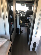 Interior of a sleek rv rental, facing the driver's cabin with a compact kitchen and living area. Ready for road trips!