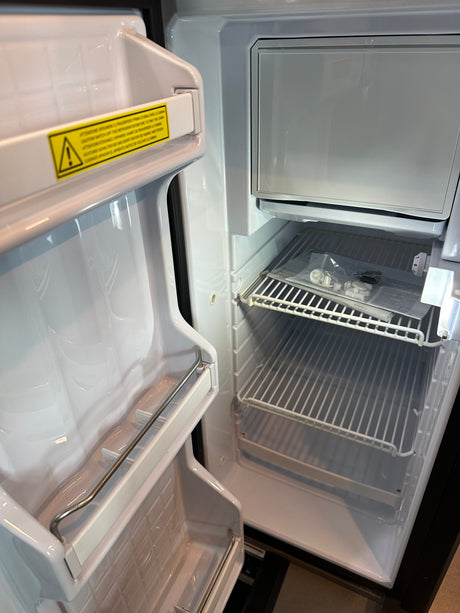 Inside a clean, compact RV rental refrigerator: open door with shelves, top freezer, wire racks, and new setup parts.