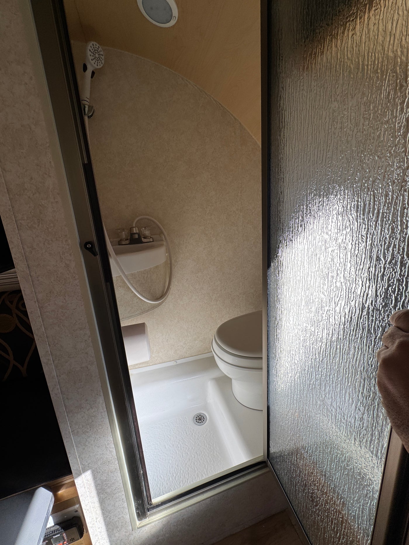 This compact RV rental bathroom features a shower, toilet, and sink, viewed through a textured glass door. — photo 15