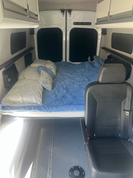 RV rental camper van interior: comfortable bed, overhead cabinets, and passenger seat, ready for travel.