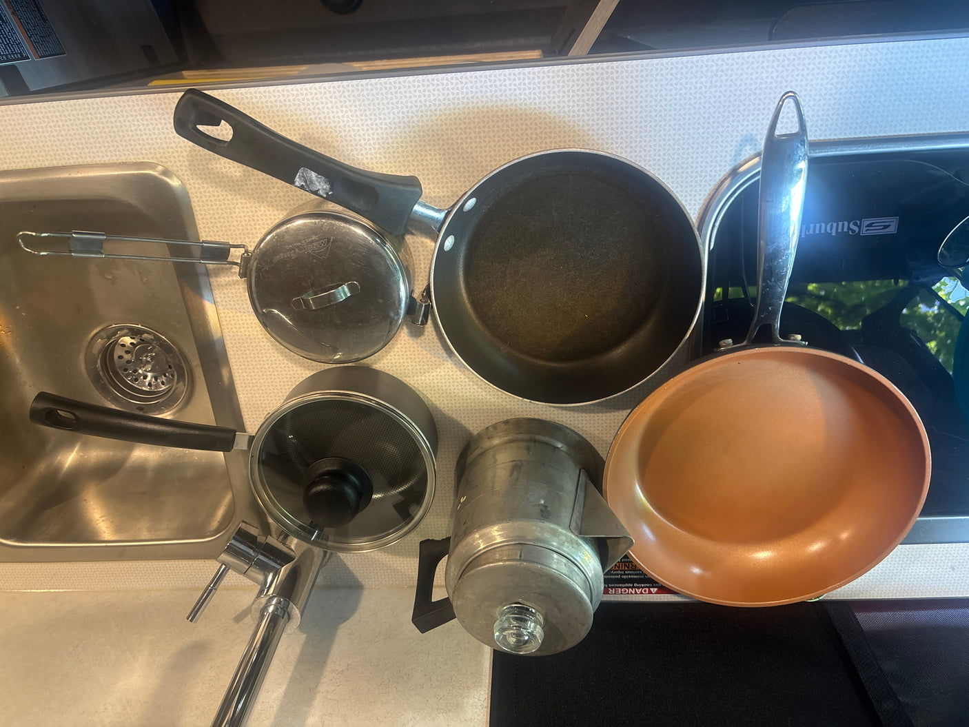 RV rental kitchen setup: Two frying pans, a pot, an MSR pot, a percolator, and a sink. Compact cooking supplies for travelers.