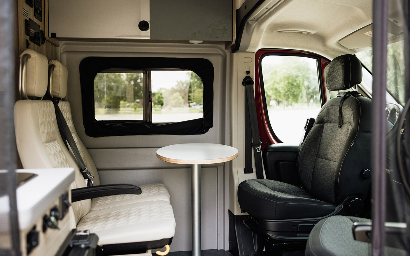 Inside this modern RV rental, see passenger and driver seats, a small table, and a window view. Ideal for travel.