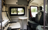 Inside this modern RV rental, see passenger and driver seats, a small table, and a window view. Ideal for travel.