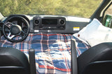 A cozy RV rental camper van interior. Plaid bedding covers the dashboard & front seats, converting the cabin into a mobile bed.