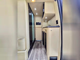 Explore this RV rental's galley: a bright kitchenette with sink, microwave, dark counter, and sleek wood-look flooring.