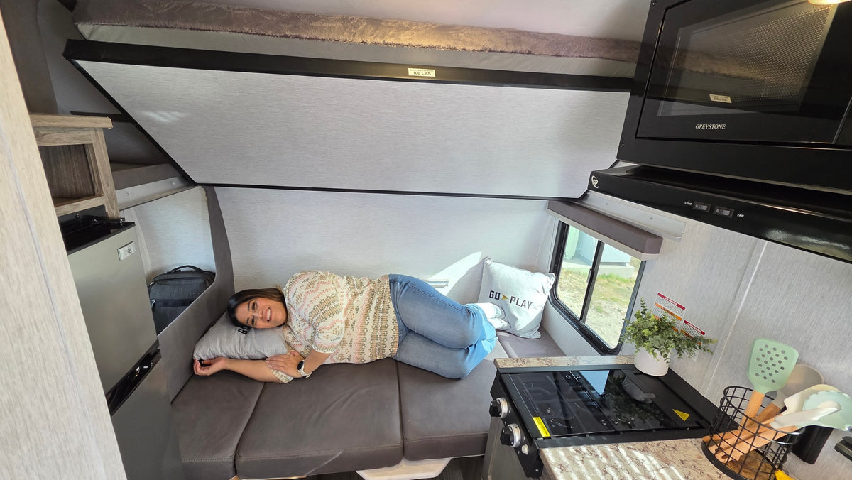 Woman relaxes inside a cozy RV rental, featuring a compact kitchen, microwave, and upper bunk bed. — photo 6