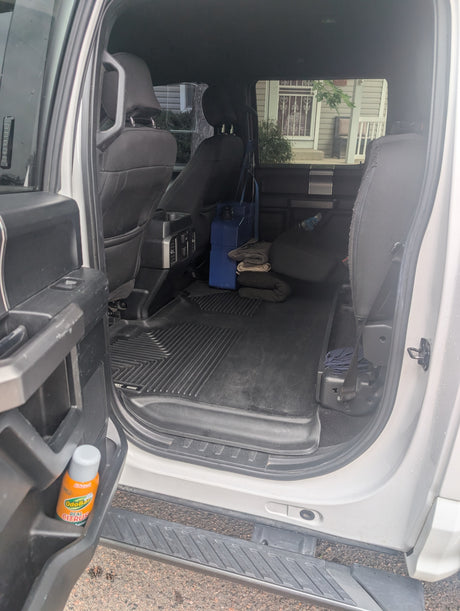 Rear interior of a large vehicle, showing flexible cargo space, floor mats, blue container, and blankets. Great for an RV rental.