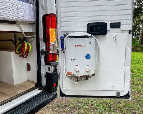 This RV rental's rear door is open, revealing a Camplux portable water heater, shower, and interior storage.