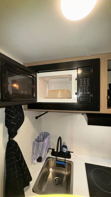 RV rental: open microwave (6:44), sink with black faucet, and electric cooktop in a compact kitchen.