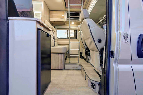 This rv rental shows a bright interior with kitchen appliances, seating, and a ladder for an overhead bed, visible from the open door.