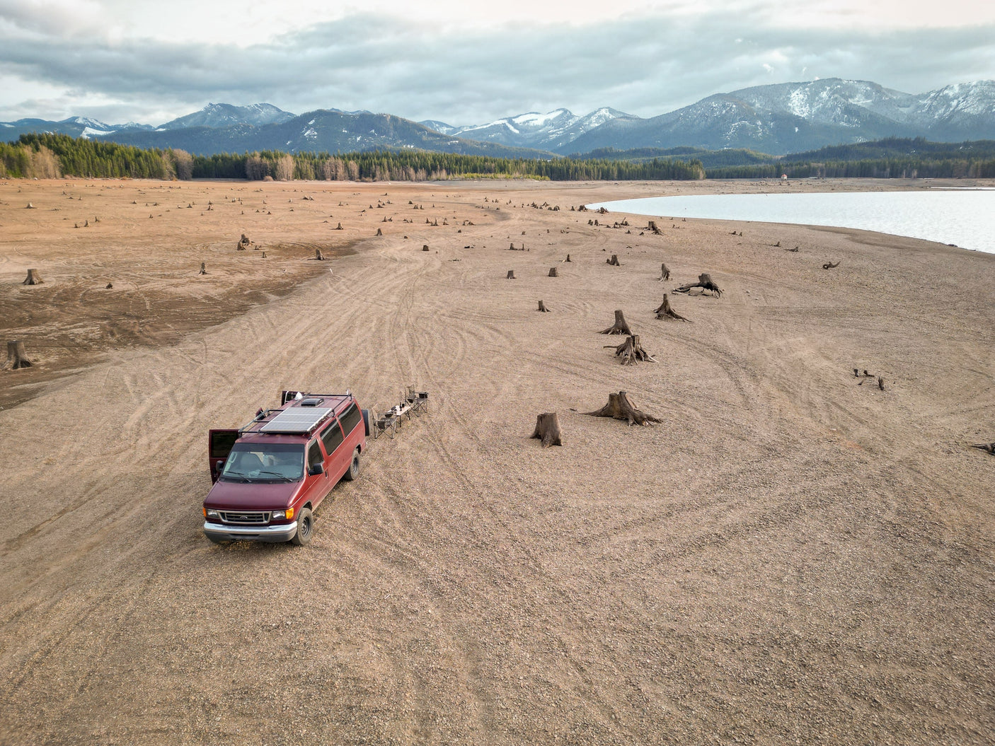 RV rental van on vast dry lakebed among tree stumps, backed by mountains. Explore unique outdoor scenery.