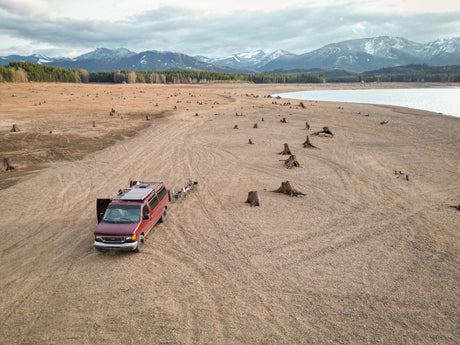 RV rental van on vast dry lakebed among tree stumps, backed by mountains. Explore unique outdoor scenery.