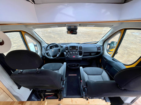 RV rental: Wide-angle view of the front cab of a customized camper van, showing the dashboard and seats.
