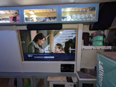  and a TV/screen setup.|Interior of an RV rental showing a full-length inflatable mattress set up as a bed across the front seats of the van.|Compact RV rental kitchen: features double stainless steel sinks — photo 8