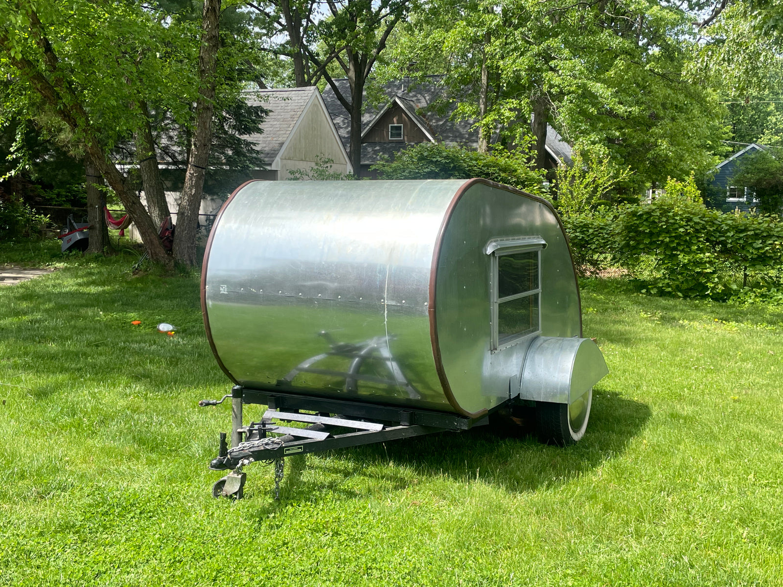 A sleek, silver teardrop trailer parked on a sunny lawn, an excellent option for a compact RV rental adventure.