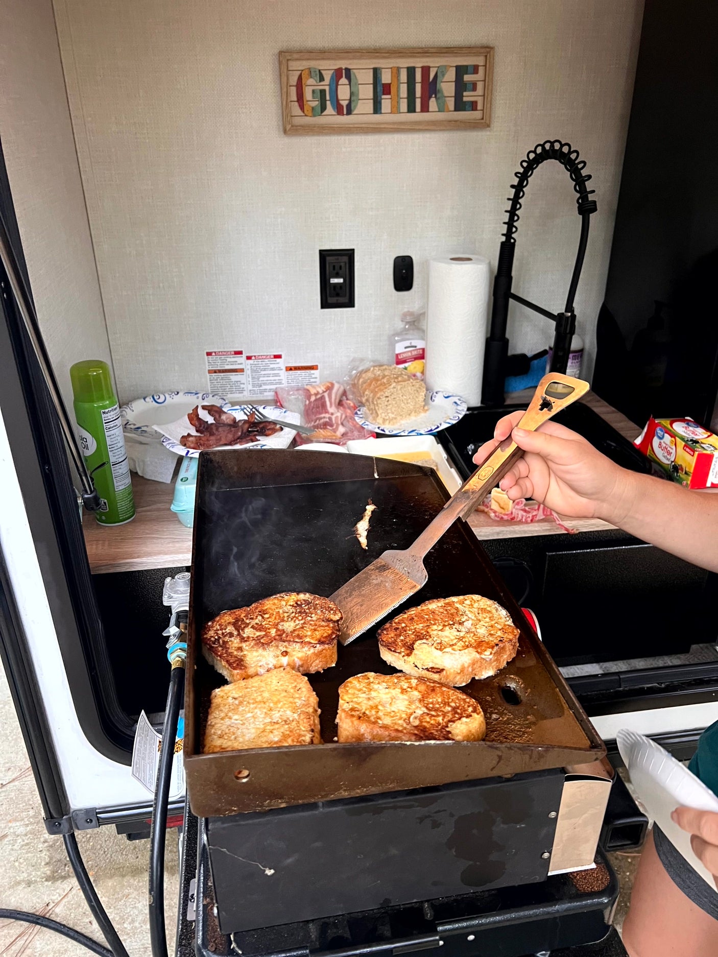 Cooking French toast and bacon on a griddle in an RV rental's outdoor kitchen. A perfect camping breakfast.