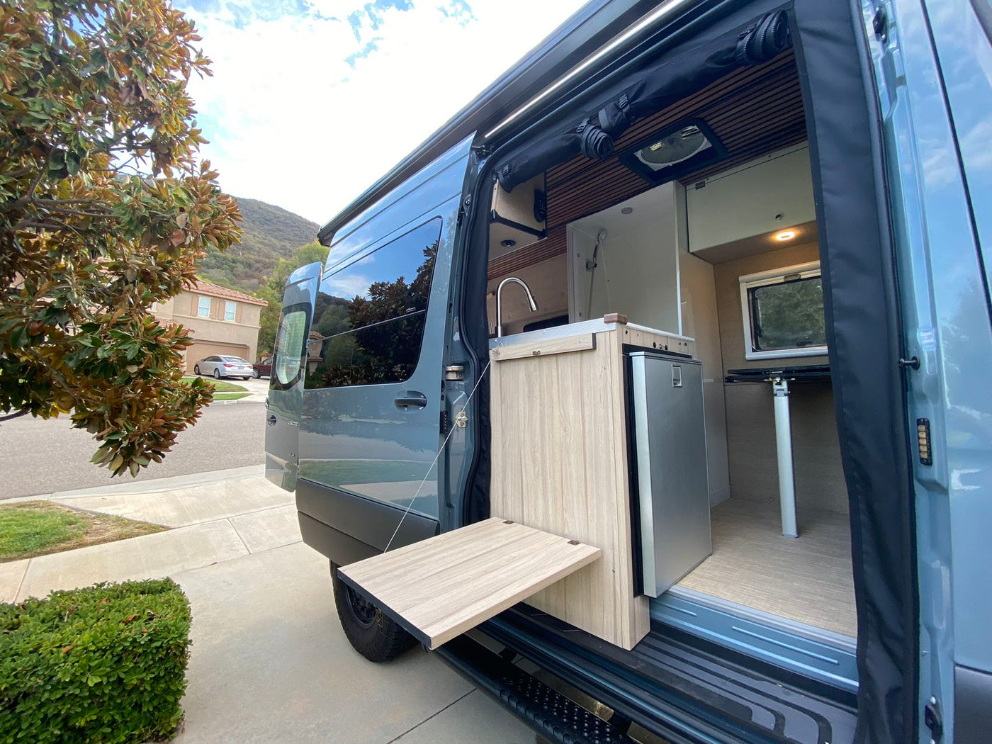  great for RV rental.|Light blue camper van with tinted windows and a side step on a driveway. Ideal for an RV rental getaway.|Gray RV rental camper van with open side door. Features mobile kitchen — photo 5