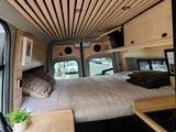 Cozy RV rental interior with a comfortable bed, wooden ceiling, and street view. Perfect for travel!