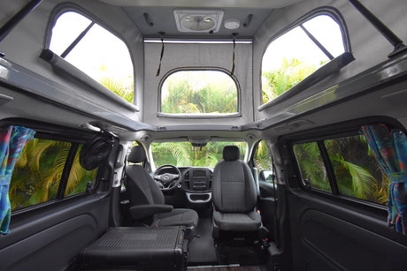 Roomy rv rental camper van interior. Features pop-top, large windows, seats, cooling fan & storage unit.