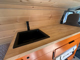 This RV rental's interior boasts a sleek kitchen: wooden wall, light wood counter with black sink/faucet, orange cabinets below.