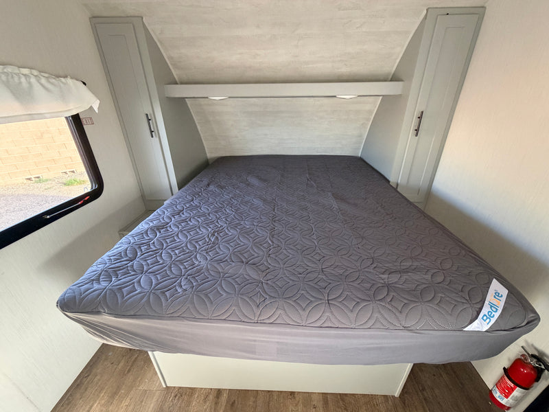 Interior of an RV rental bedroom features a grey quilted bed, overhead storage, window with EXIT sign, and a fire extinguisher. — photo 2