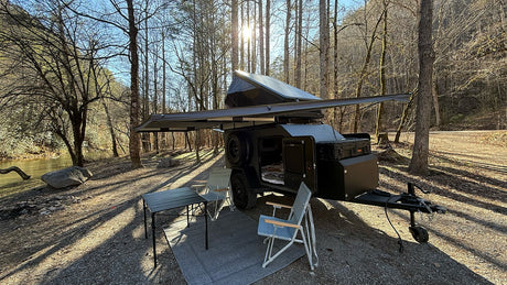Riverside rv rental campsite with an off-road camper trailer, awning, table, & chairs. Perfect nature escape.