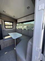 Modern RV rental interior with a spacious U-shaped dinette, marble-top table, and large windows.