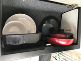 RV rental kitchen: white dishes, red pots, & cutting board neatly organized in a compact, felt-lined cabinet.