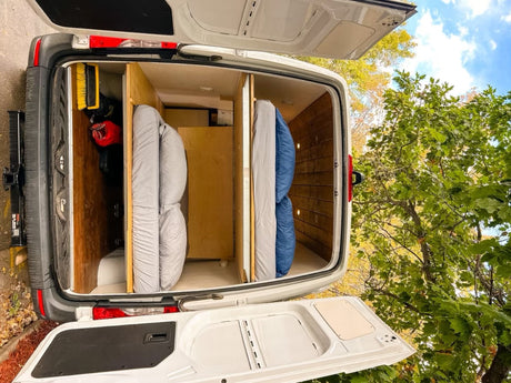 Rear view of an RV rental's camper van interior, featuring two rolled mattresses and wood storage.