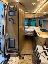 The interior of this RV rental shows a compact kitchen, bed, and control panel, designed for efficient mobile living.