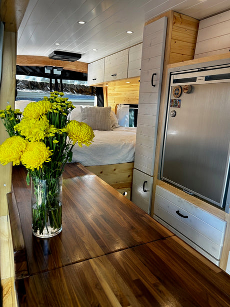 RV rental interior: custom wood counters, bright white cabinets, stainless fridge, and a comfy bed. Perfect for van life.