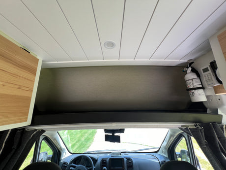 RV rental interior showcasing an elevated sleeping area, crisp white ceiling, and front cabin with dashboard.