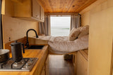 Experience van life in this cozy RV rental: kitchen, bed, and stunning ocean views out the back window.