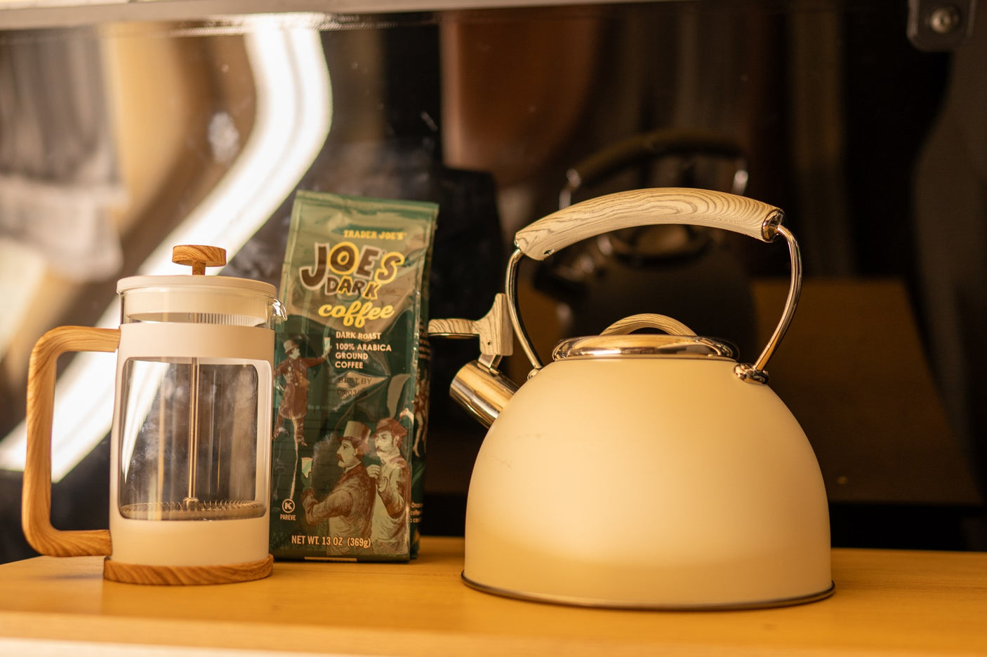 A French press, light-colored kettle, and Trader Joe's coffee bag on a wooden surface, ready for coffee on your rv rental trip.