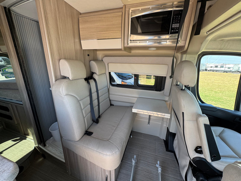 Inside an rv rental van: light-colored dinette seats, a wall-mounted microwave, and a folding table, ready for travel. — photo 5