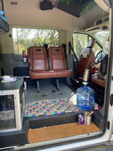 Spacious RV rental interior: brown leather seats, utility station with battery, water dispenser, and colorful floor mats.