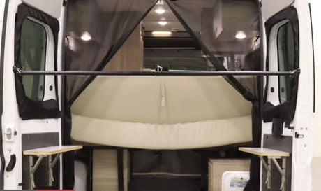 Rear view of an RV rental: open doors reveal a comfortable van bed, mosquito screen, and portable tables.
