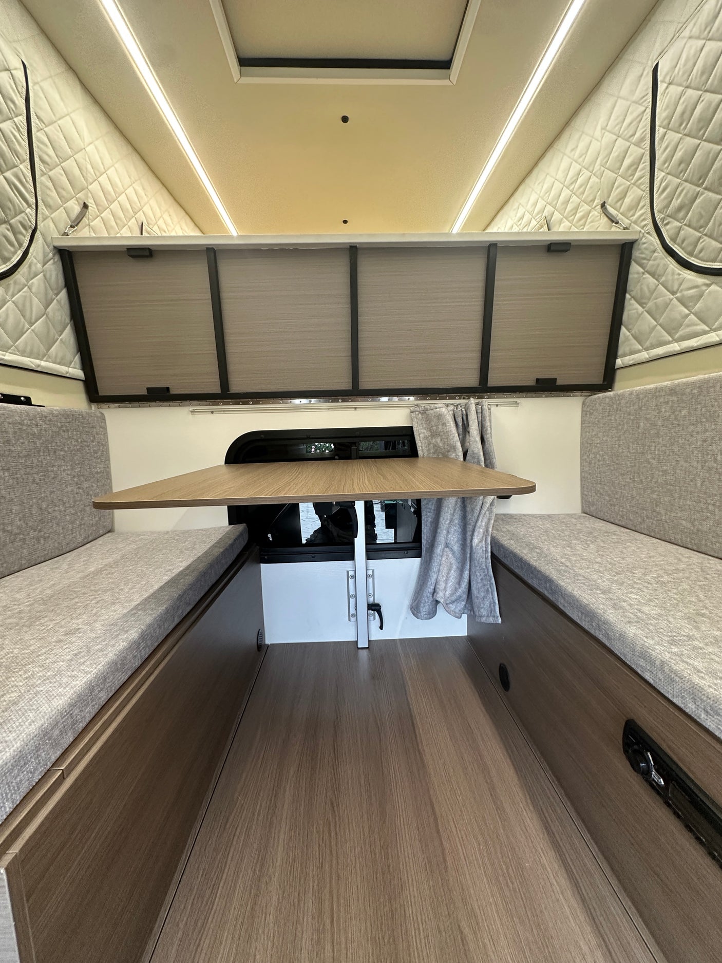 Interior of a clean **rv rental** showing a dinette with grey cushioned benches, wood table, overhead storage, and bright LED lighting.