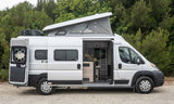 A silver pop-top camper van with its side door open, showing the cozy interior. An ideal RV rental for road trips.