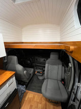 RV rental van conversion interior with a built-in wooden platform above the front cabin and white paneling.
