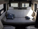 RV rental interior: A light-colored bench seat, convertible to a bed, with two pillows, flanked by windows. Ideal camper van comfort.