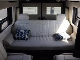RV rental interior: A light-colored bench seat, convertible to a bed, with two pillows, flanked by windows. Ideal camper van comfort. — photo 12
