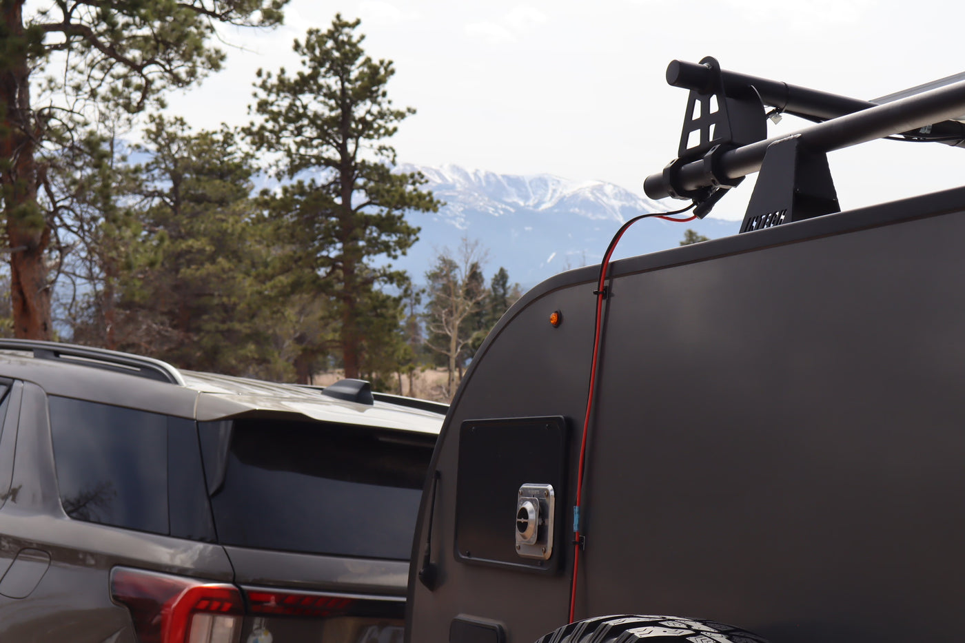 RV rental: Teardrop trailer & SUV parked, ready for mountain camping. Snowy peaks & pine trees line the horizon. — photo 10