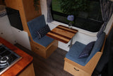 Cozy RV rental interior showcasing a compact dining area with blue benches, a wooden table, and an integrated kitchen.